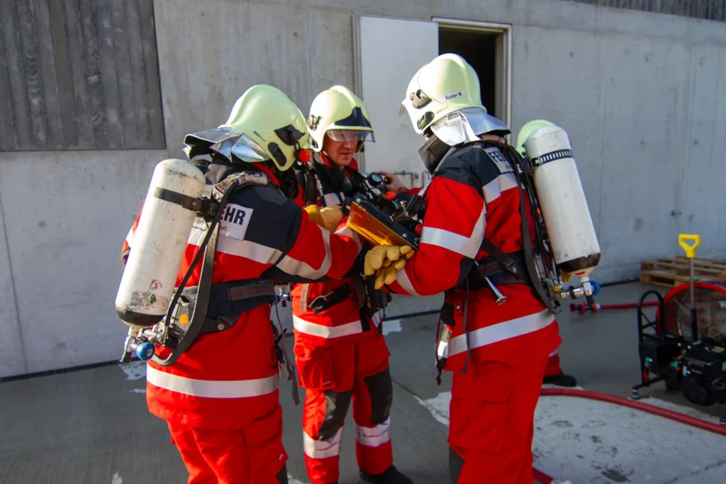 Firefighters in protective gear examine equipment during a training exercise outdoors.