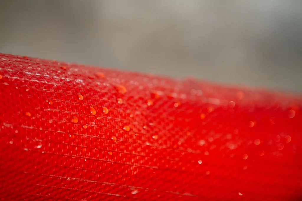 Close-up of red textured fabric with glistening water droplets, detailed pattern.