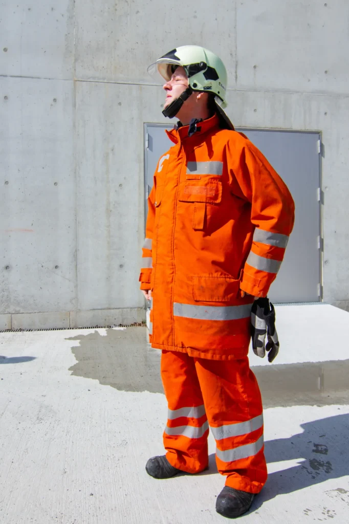 Firefighter in orange protective gear and helmet looking upwards, ready for action.